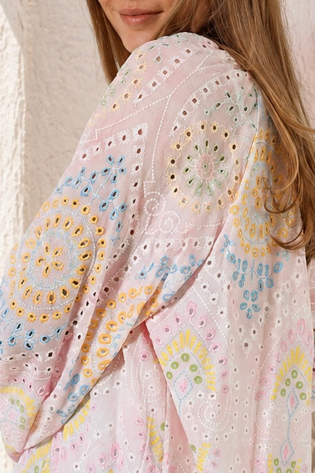 A close-up of a woman wearing a light pink eyelet embroidered top with pastel multicolor mandala and floral patterns.