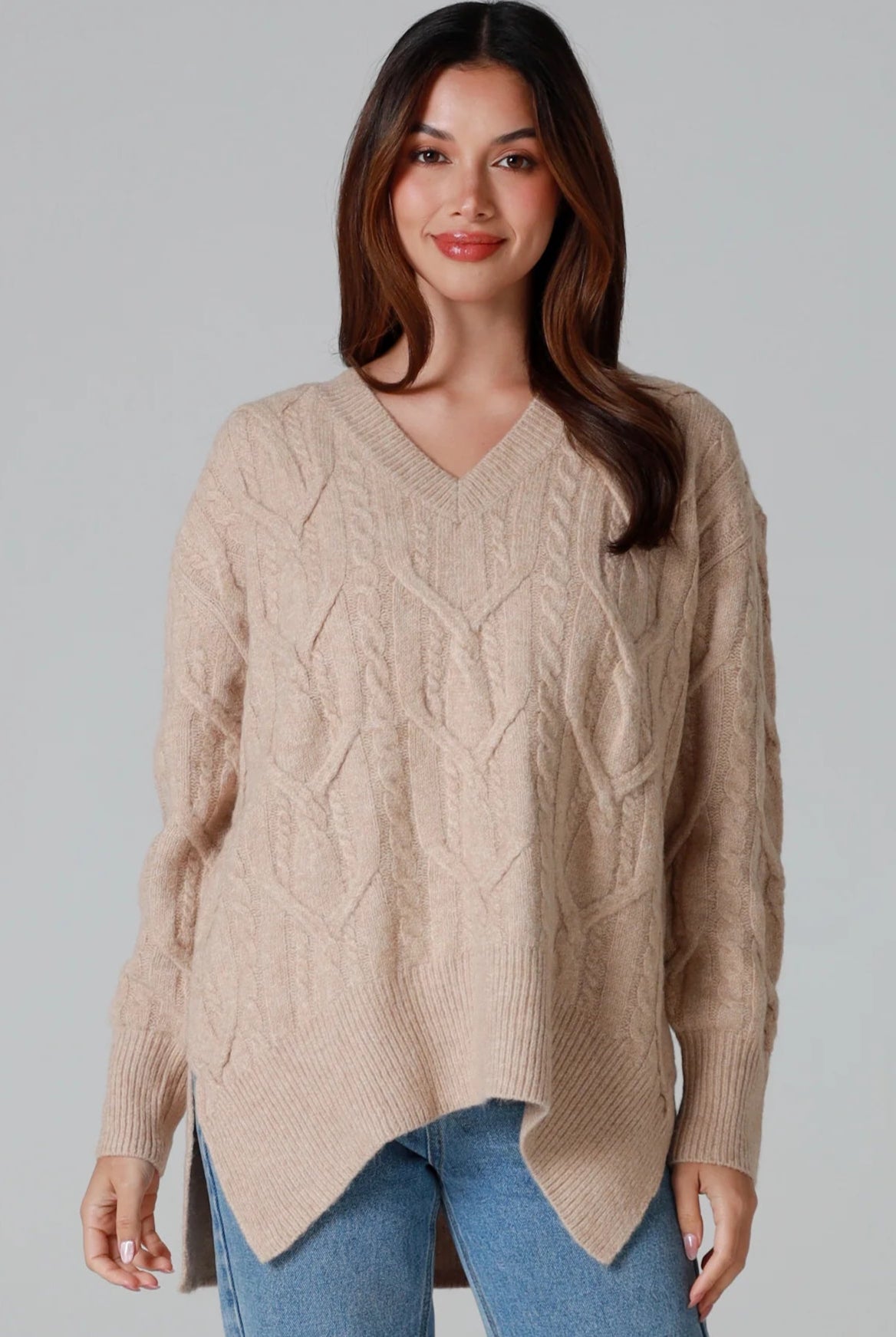 Woman wearing a biscotti colour wool blend cable knit jumper with relaxed fit and v-neckline - Caldra Knit Jumper Australia.