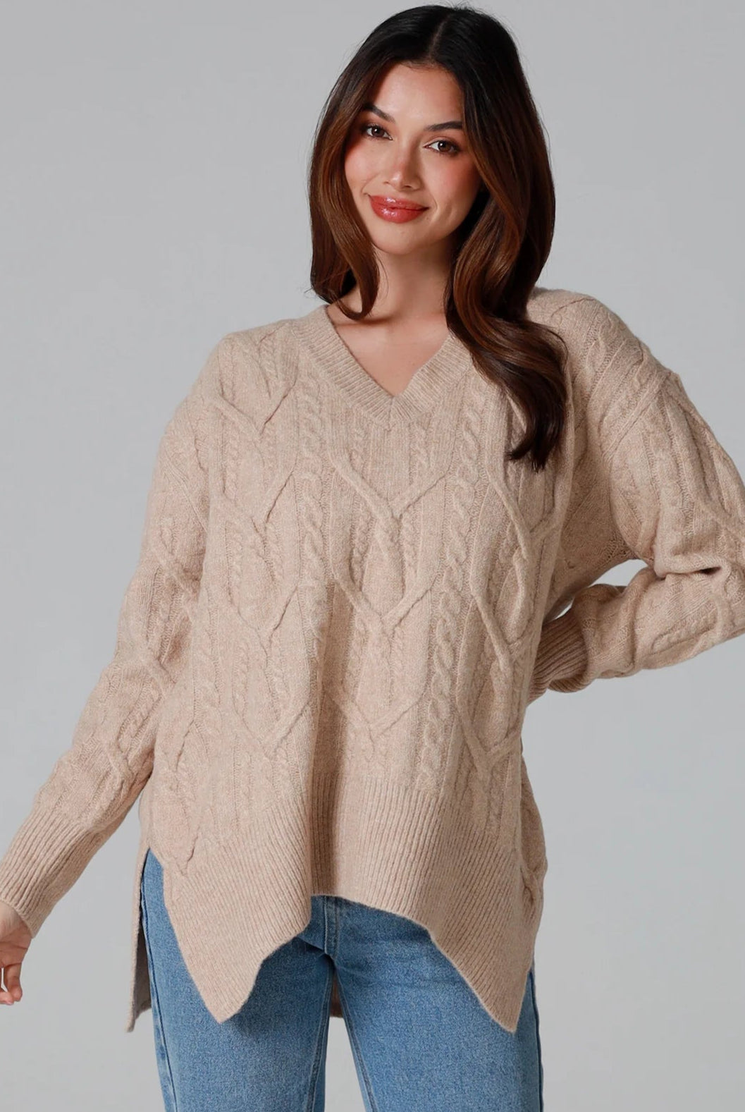 Woman wearing a biscotti colour wool blend cable knit jumper with relaxed fit and v-neckline - Caldra Knit Jumper Australia.
