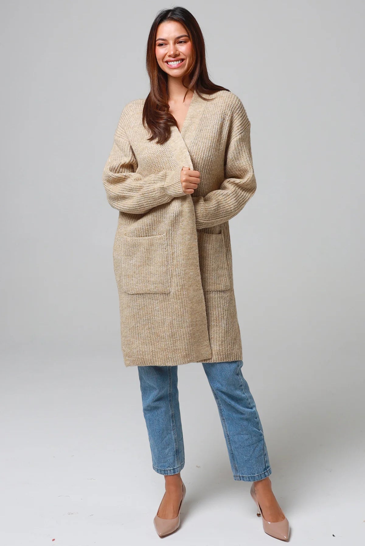 Woman wearing a beige longline knit cardigan with front pockets and jeans - neutral boho knitwear Australia.