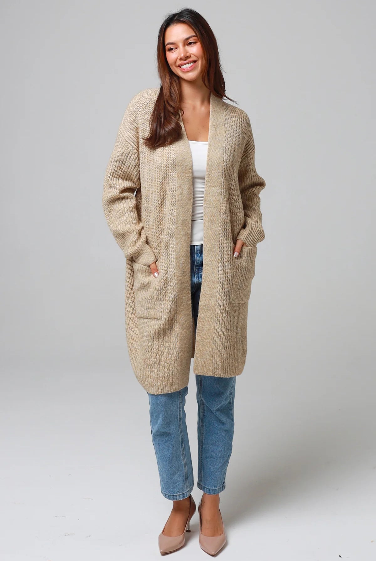 Woman wearing a beige longline knit cardigan with front pockets and jeans - neutral boho knitwear Australia.