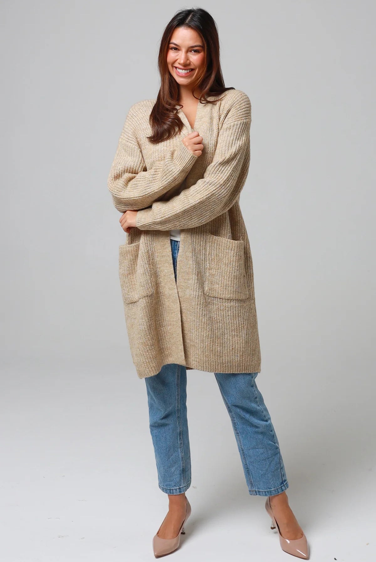 Woman wearing a beige longline knit cardigan with front pockets and jeans - neutral boho knitwear Australia.
