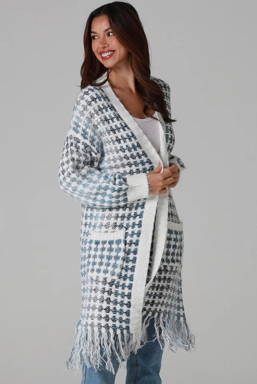 Woman wearing Juliet white and blue houndstooth longline fringe knit cardigan with drop shoulder sleeves, ribbed cuffs and front pockets by Charlotte The Label.