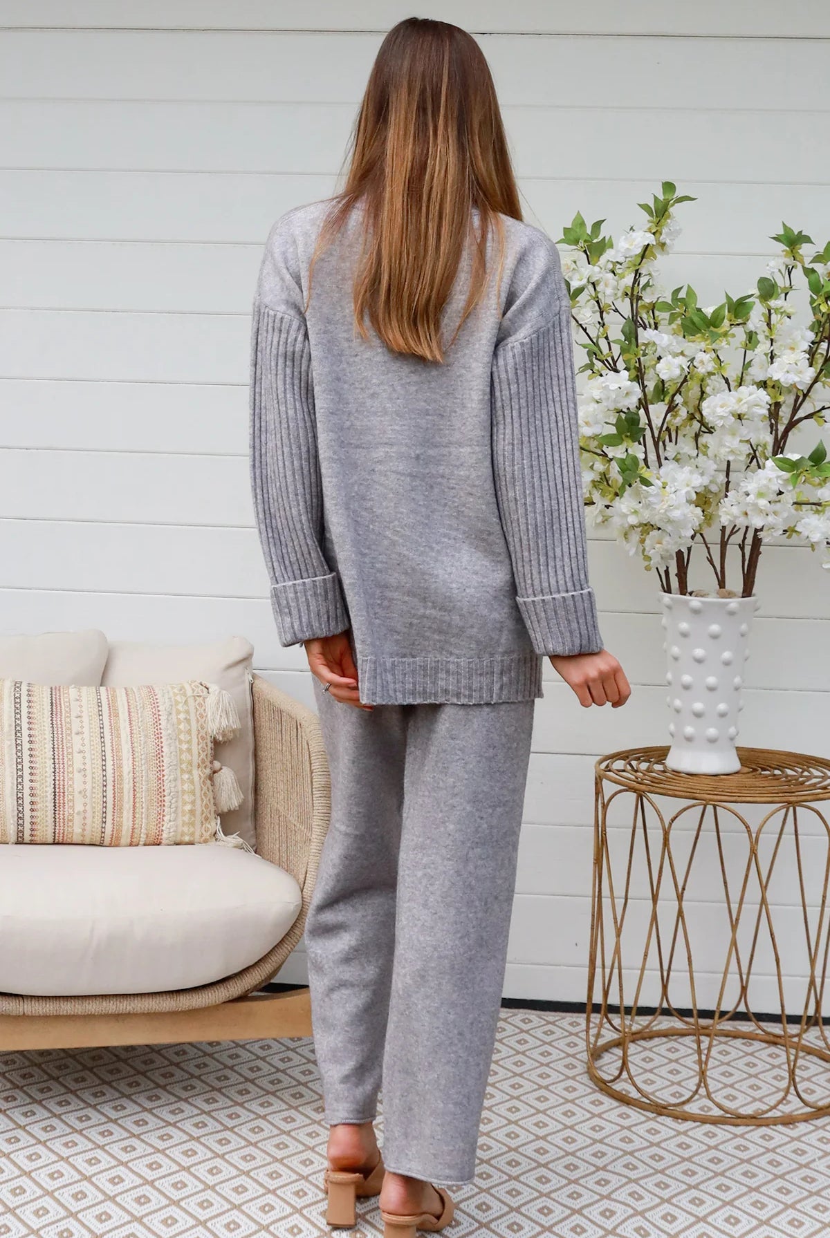 Woman wearing grey knit lounge set with high-neck jumper and wide-leg pants standing in front of a white timber wall - Mellow Lounge Set Grey Mist Bohemian Love Runway