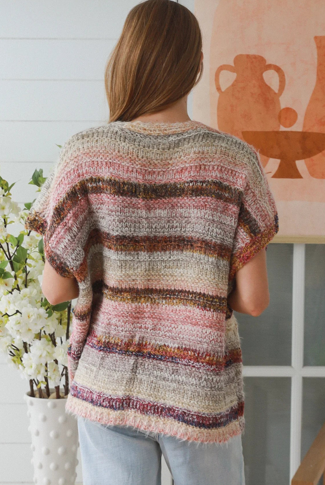 Woman wearing blush marled knit vest with textured finish layered over white top in natural indoor light