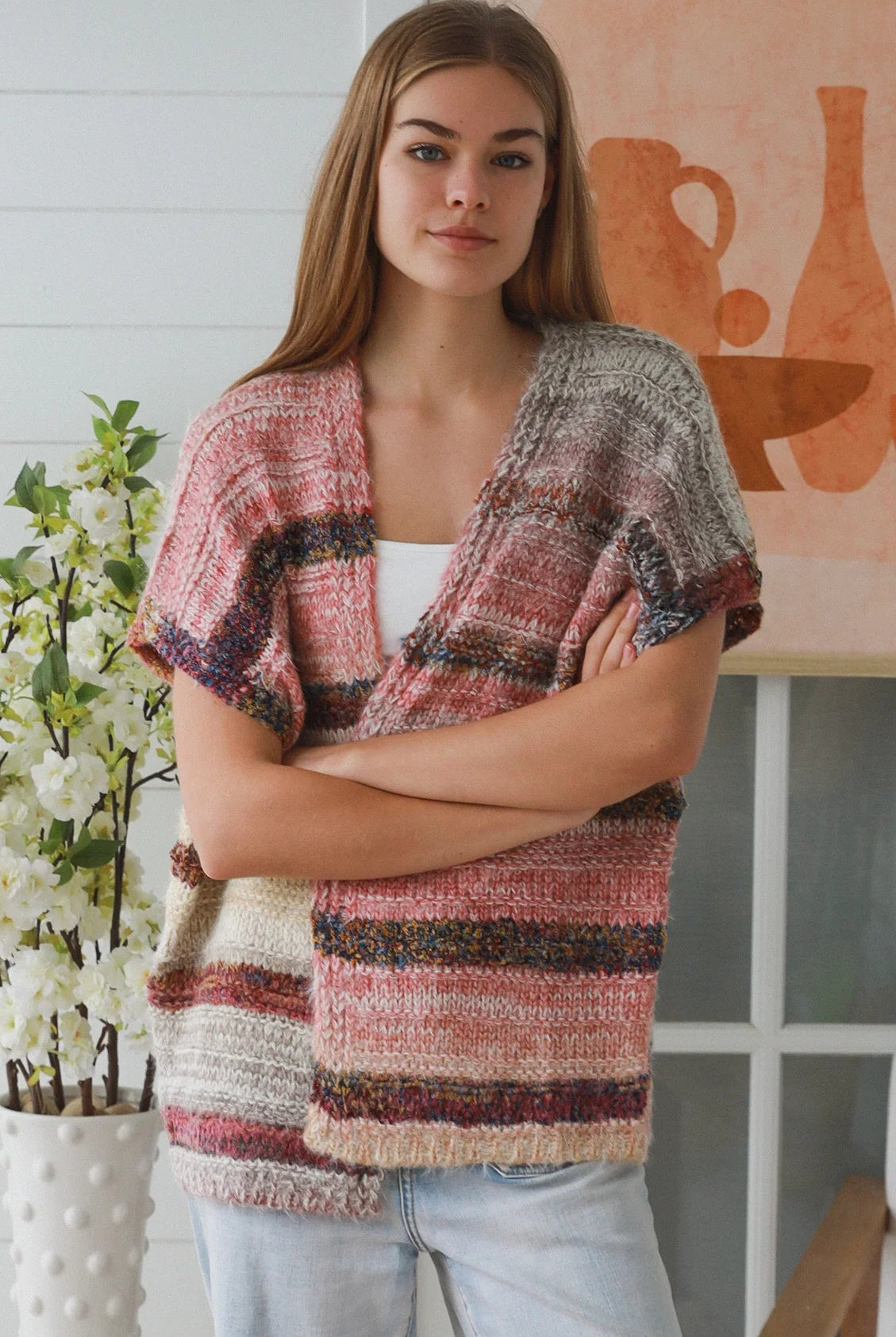 Woman wearing blush marled knit vest with textured finish layered over white top in natural indoor light