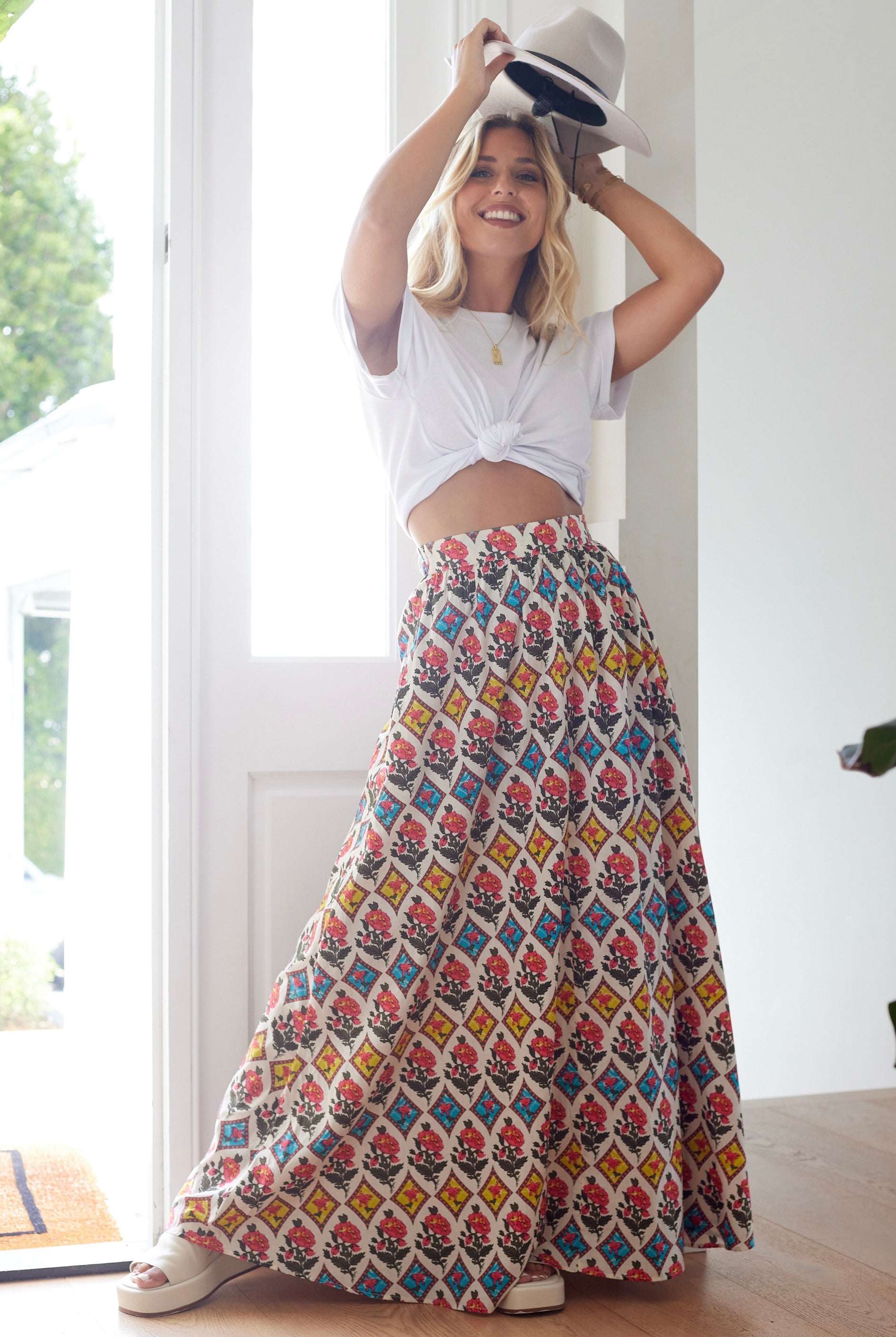 Woman wearing a colorful patterned skirt and white top indoors.