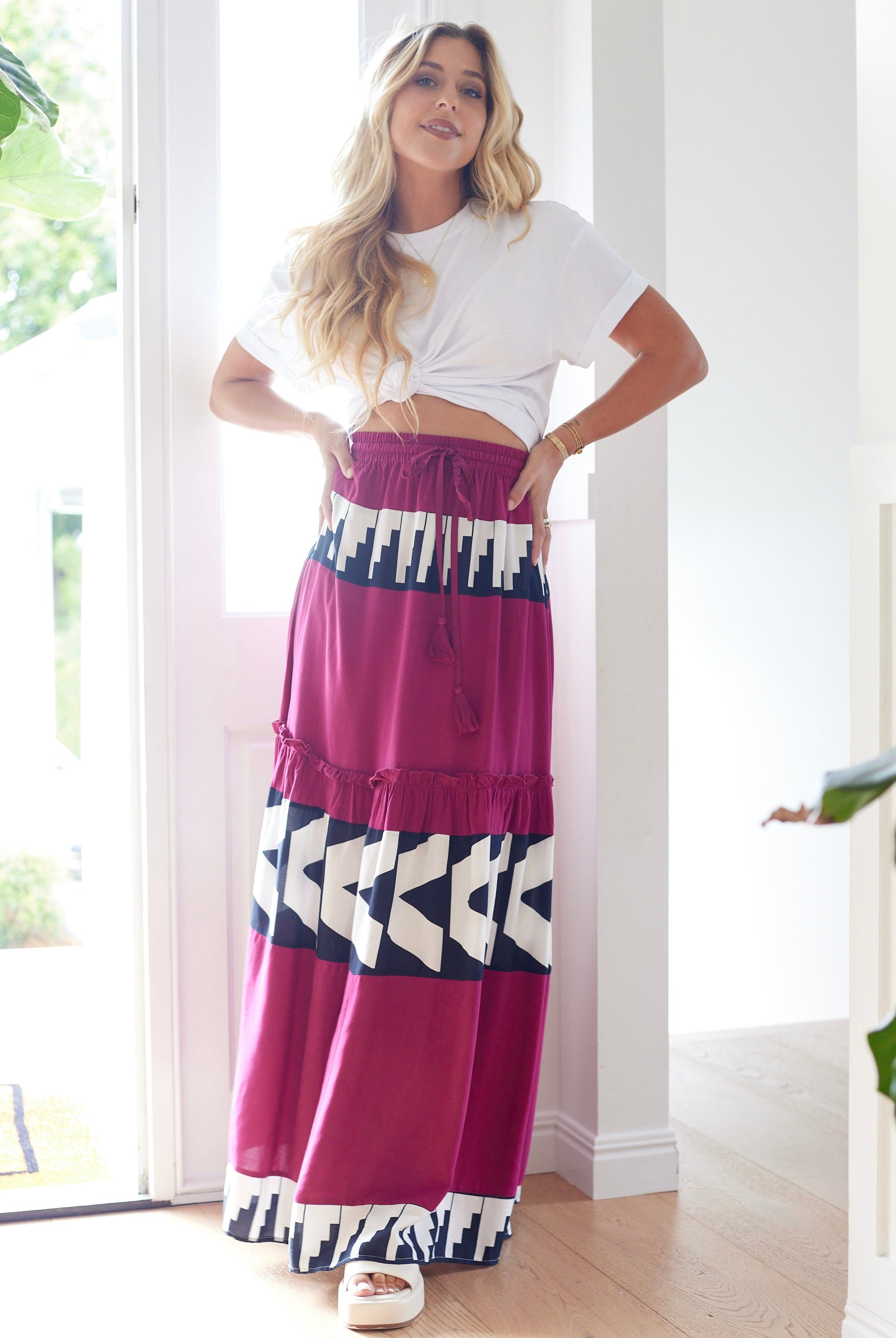 Woman wearing a white crop top and a long, patterned skirt indoors.