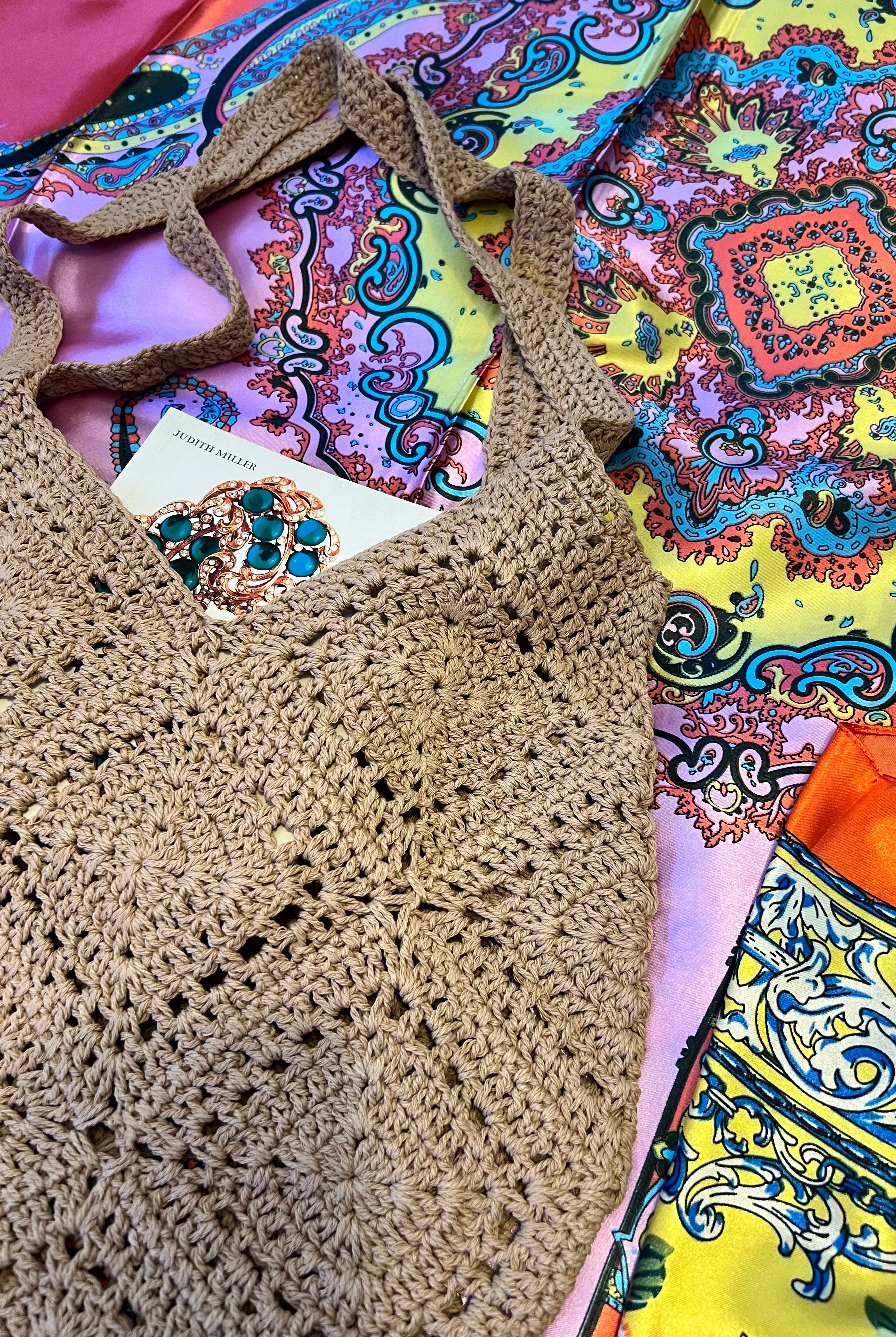 Tan crochet shoulder bag laid flat on a vibrant boho scarf background - artisan-style boho accessory Australia.