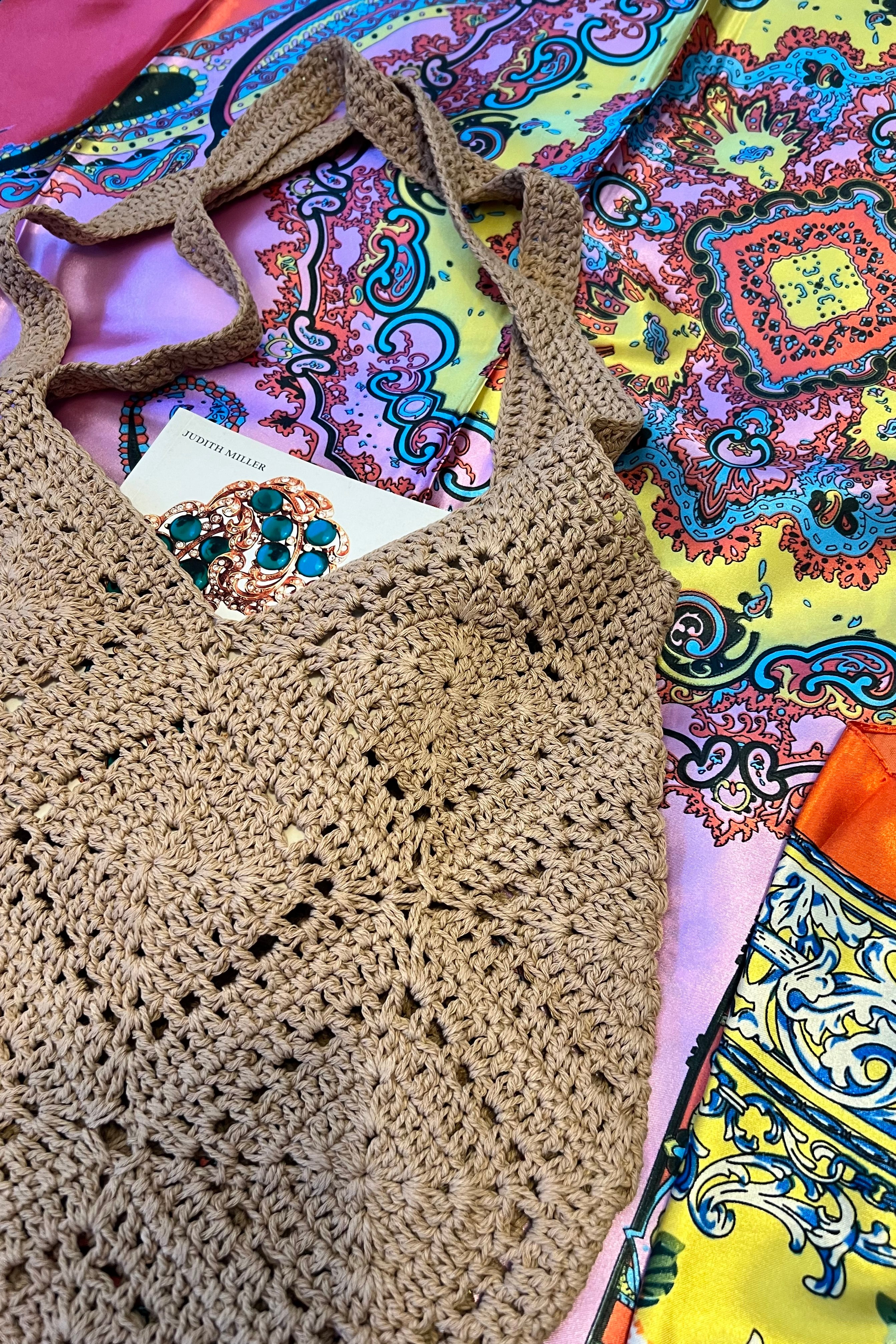 Tan crochet shoulder bag laid flat on a vibrant boho scarf background - artisan-style boho accessory Australia.