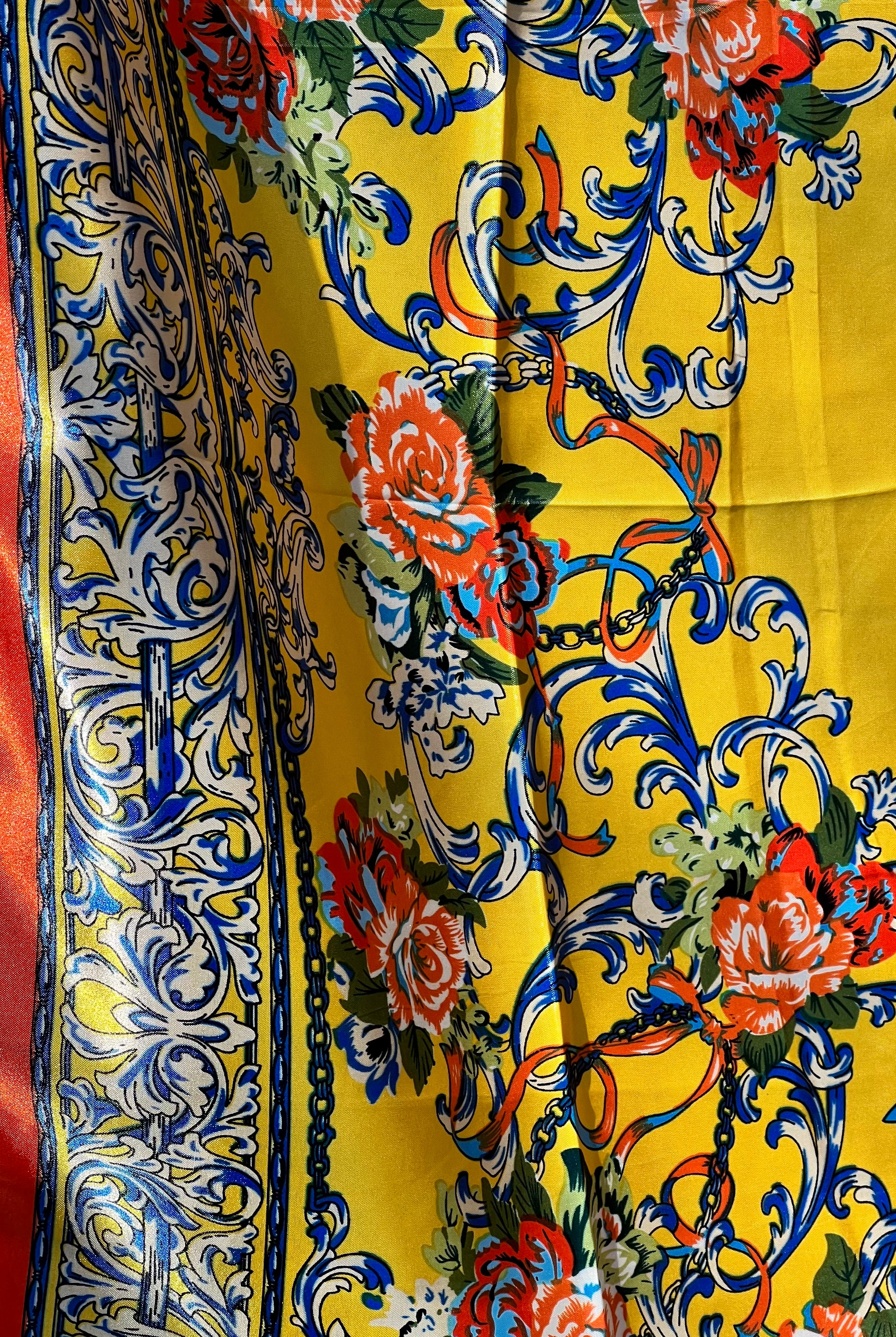 Yellow satin scarf with blue baroque scrolls and red floral print draped in sunlight - boho satin scarves Australia.