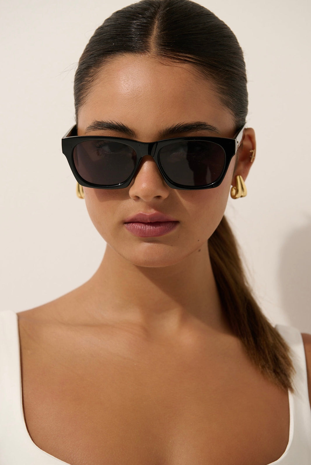 Woman wearing black square boho sunglasses with gold earrings and slick ponytail - vintage summer fashion Australia