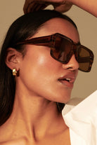 Woman in brown vintage square sunglasses with gold earrings and white shirt - tonal boho style Australia.