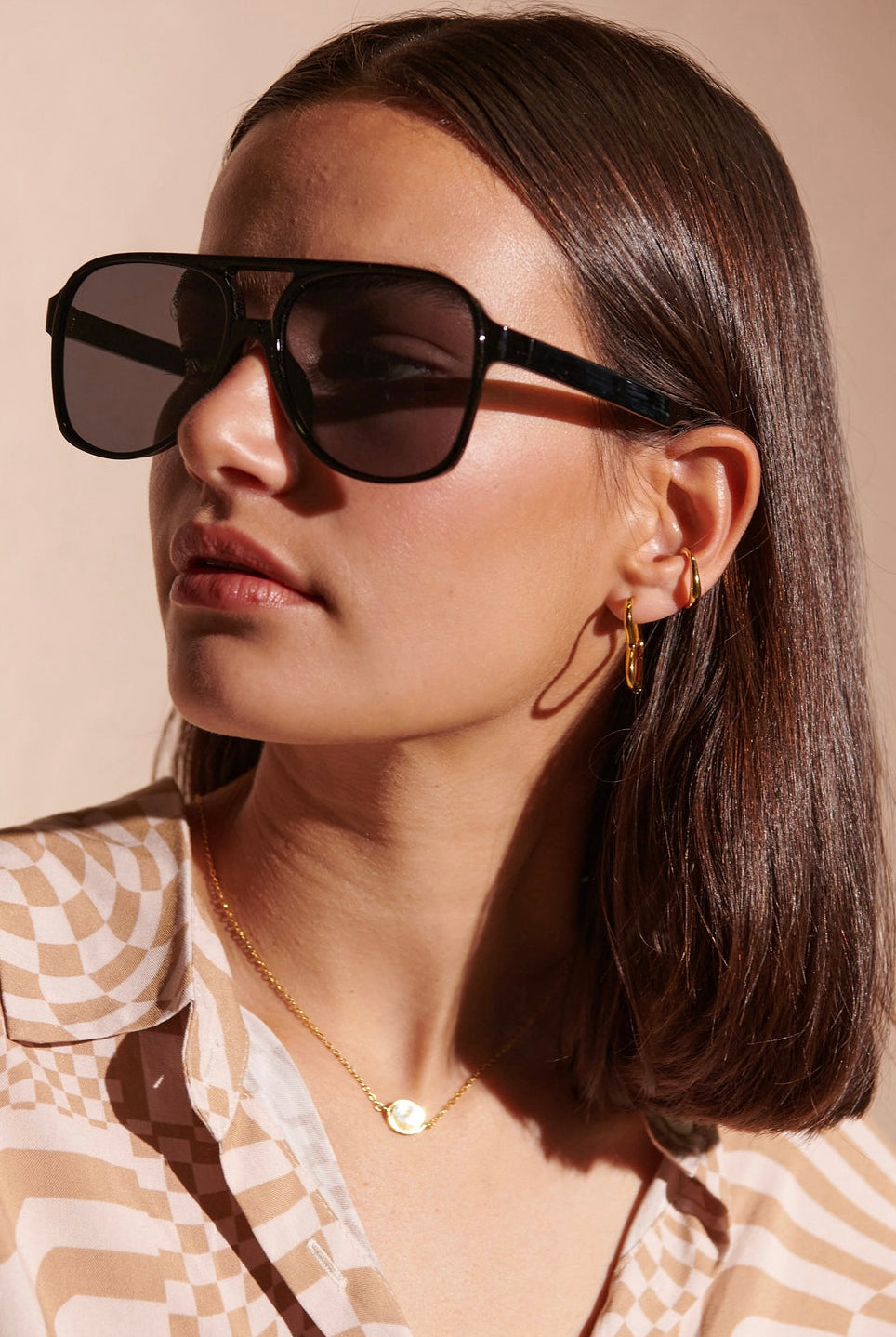 Woman in oversized black sunglasses with gold hoop earrings and patterned blouse - modern boho street style Australia.