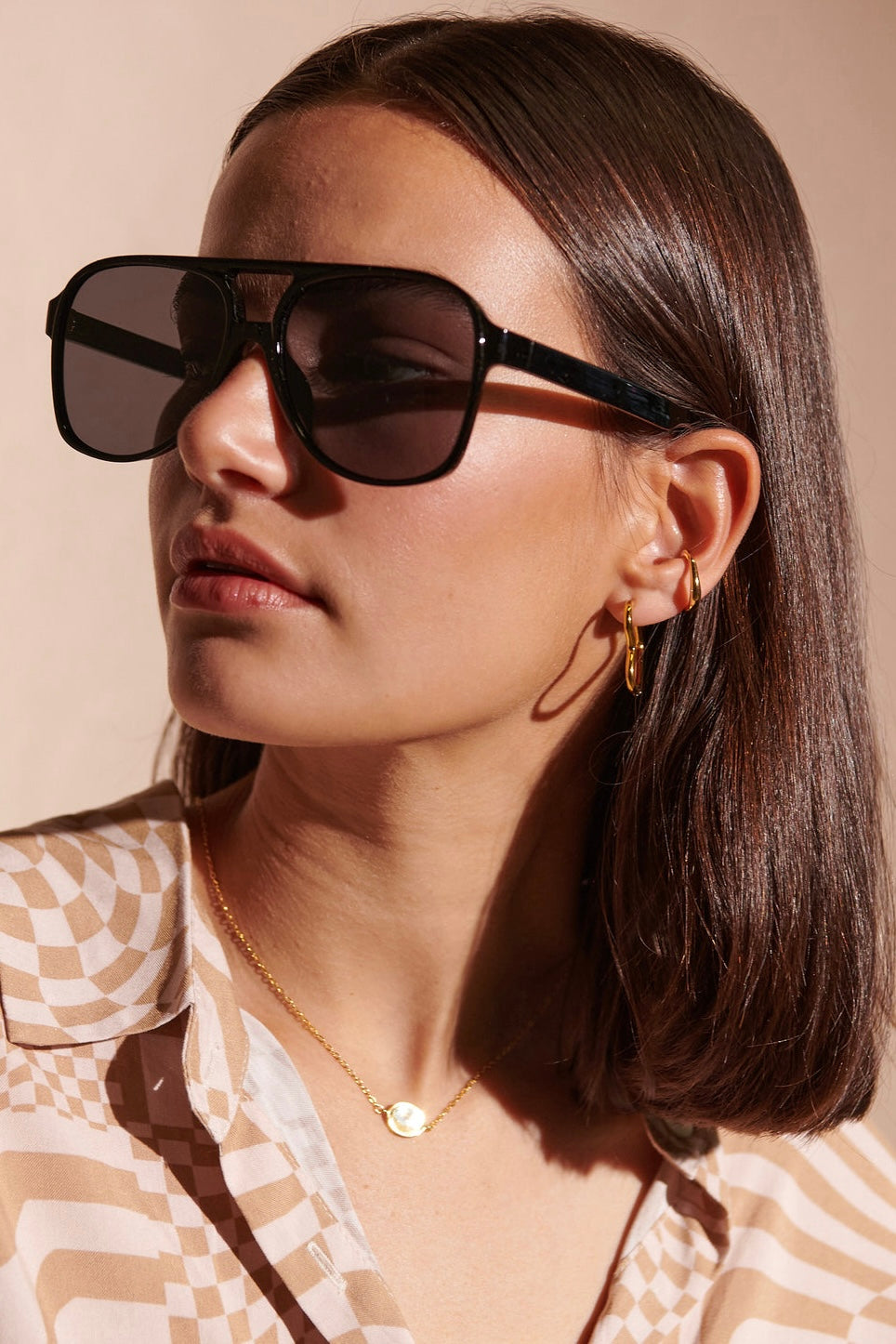 Woman in oversized black sunglasses with gold hoop earrings and patterned blouse - modern boho street style Australia.