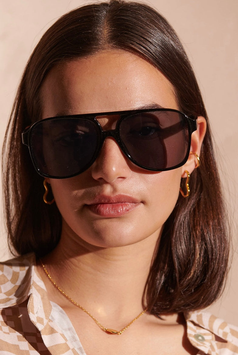 Woman in oversized black sunglasses with gold hoop earrings and patterned blouse - modern boho street style Australia.