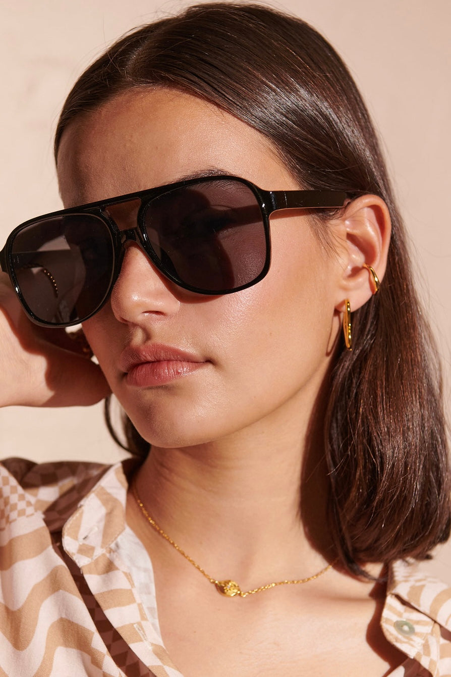 Woman in oversized black sunglasses with gold hoop earrings and patterned blouse - modern boho street style Australia.