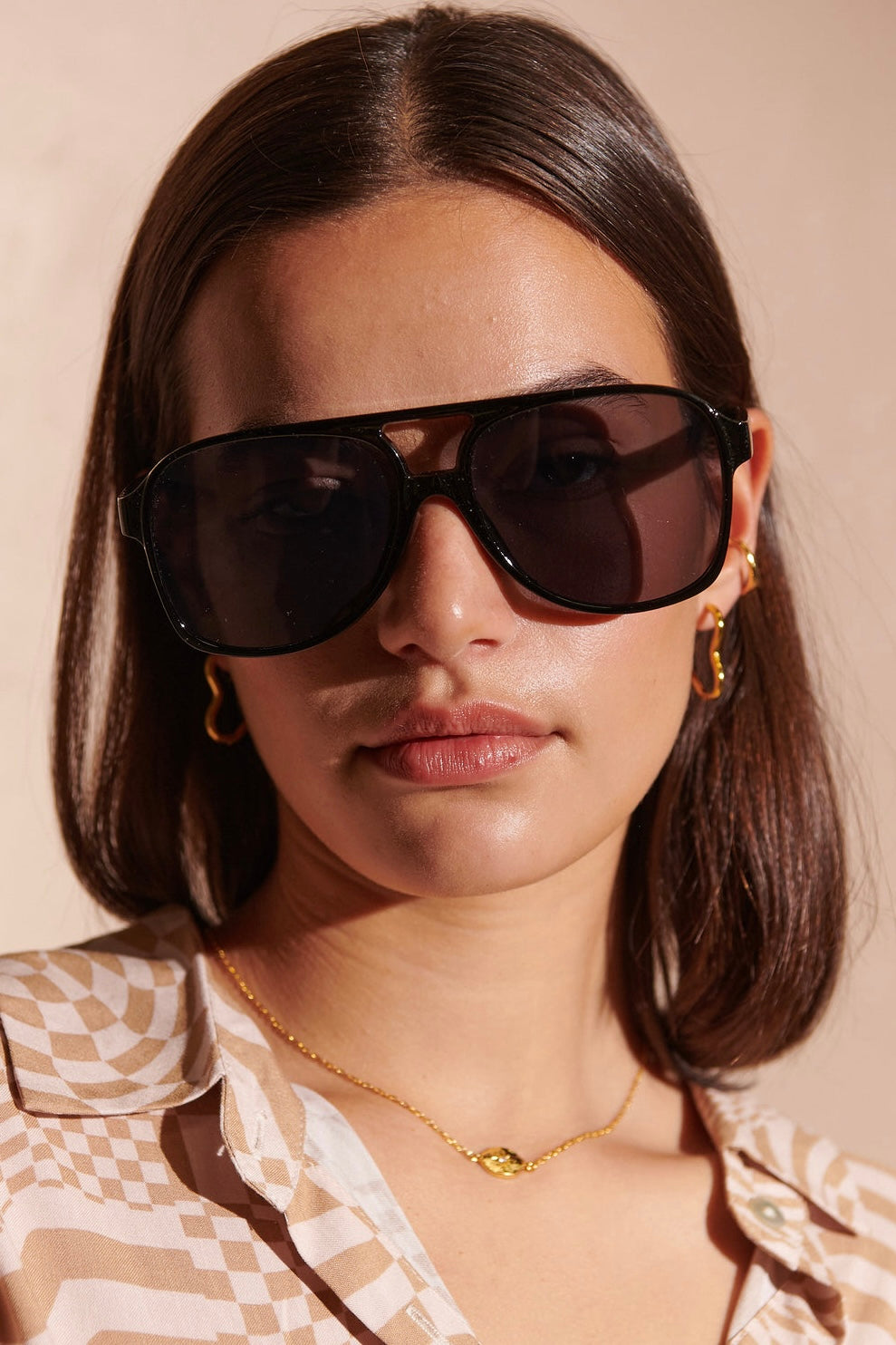 Woman in oversized black sunglasses with gold hoop earrings and patterned blouse - modern boho street style Australia.