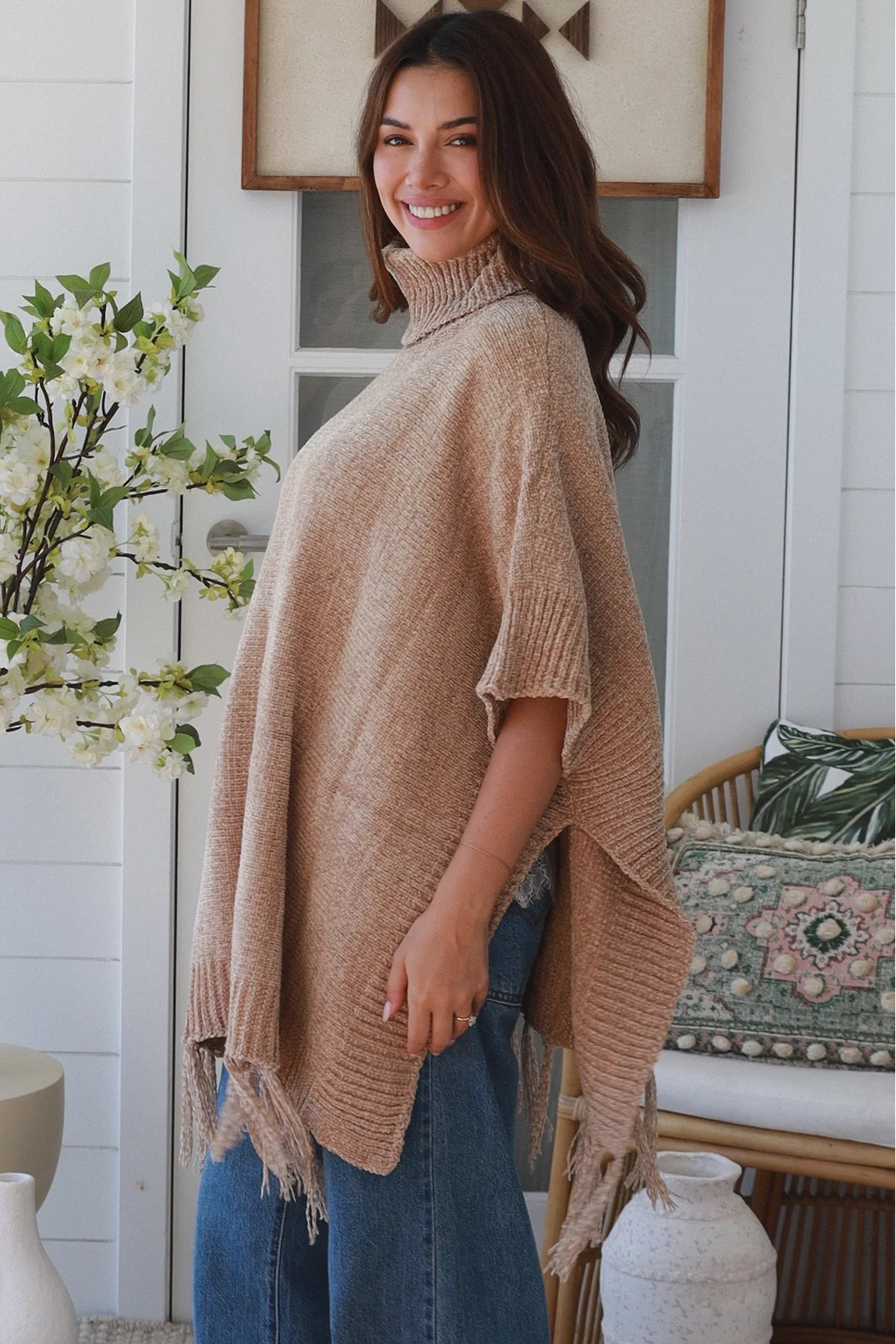 Warm oat roll neck knit poncho with fringe hem draped winter layering piece styled over fitted long sleeve neutral outfit Australia