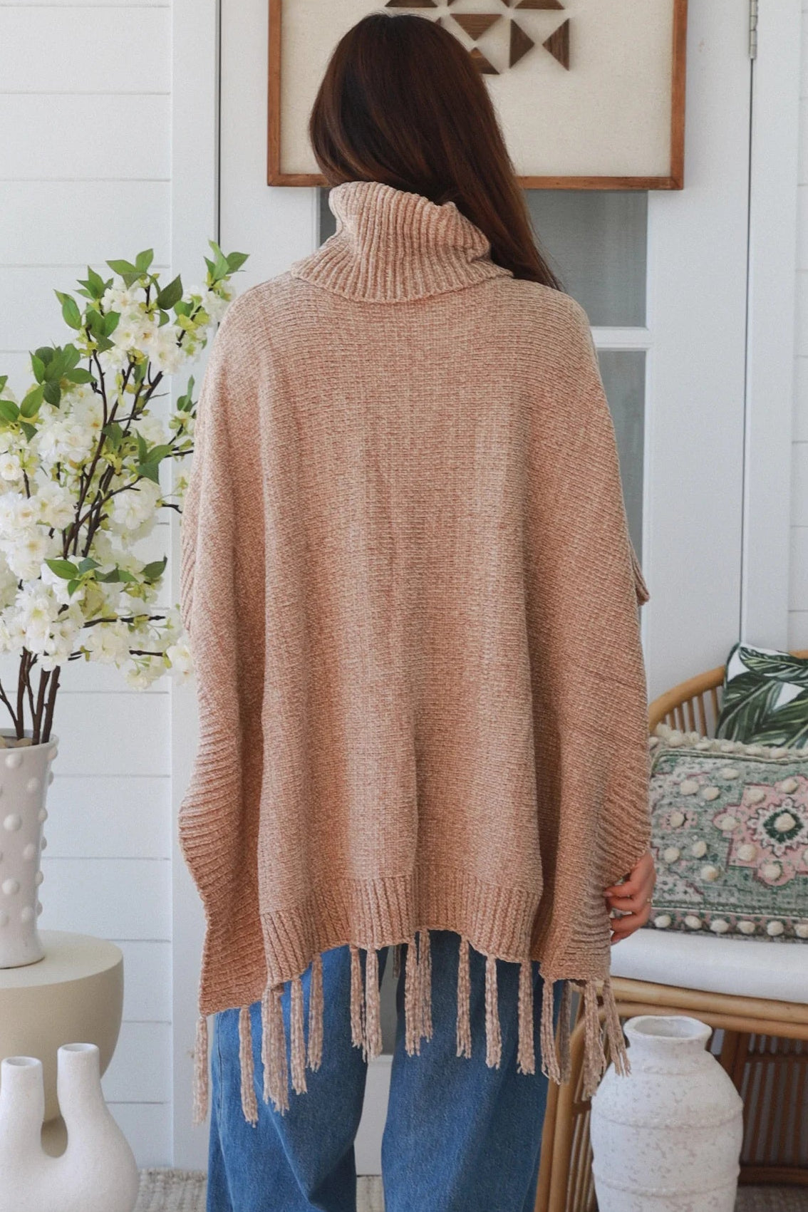 Warm oat roll neck knit poncho with fringe hem draped winter layering piece styled over fitted long sleeve neutral outfit Australia