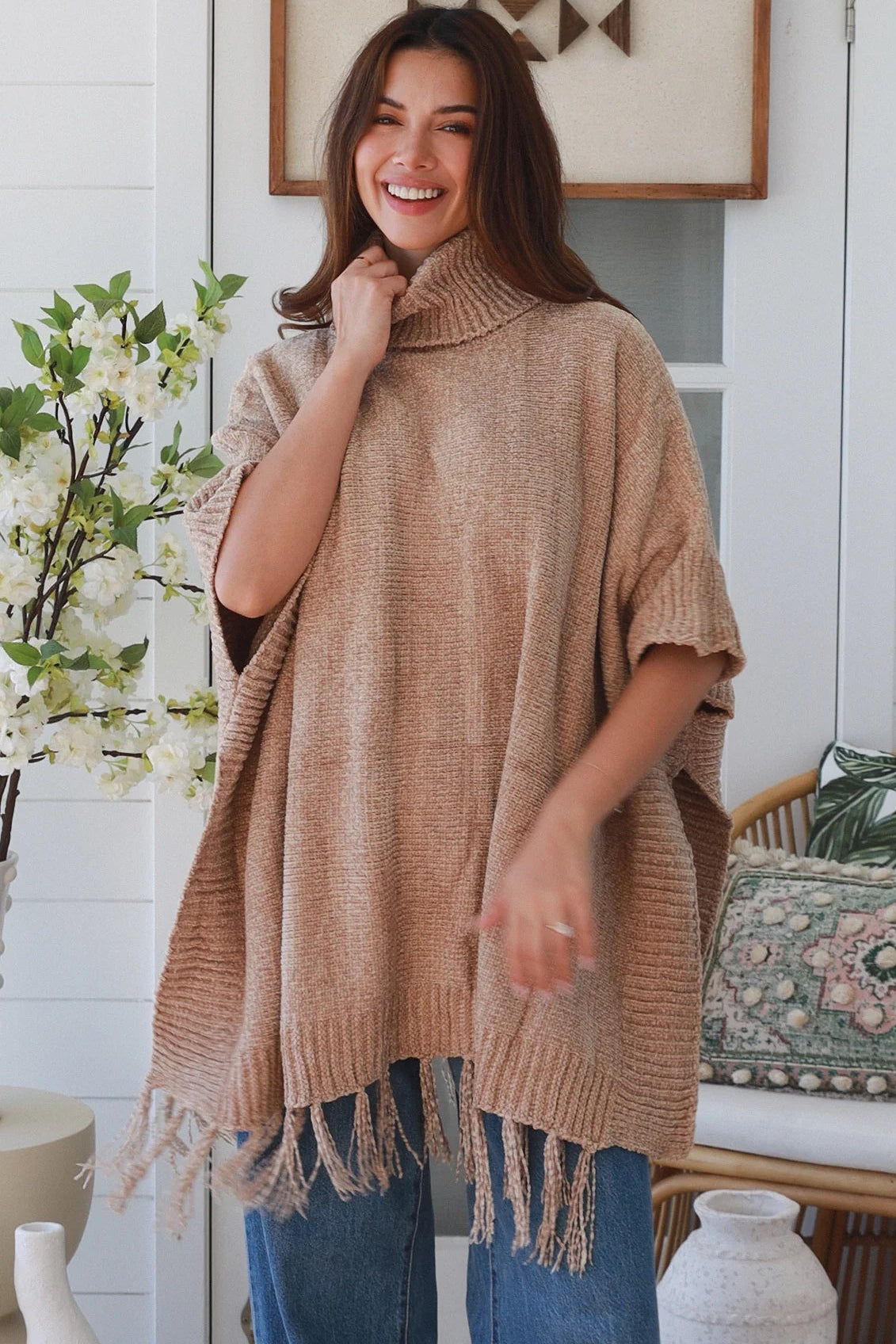 Warm oat roll neck knit poncho with fringe hem draped winter layering piece styled over fitted long sleeve neutral outfit Australia