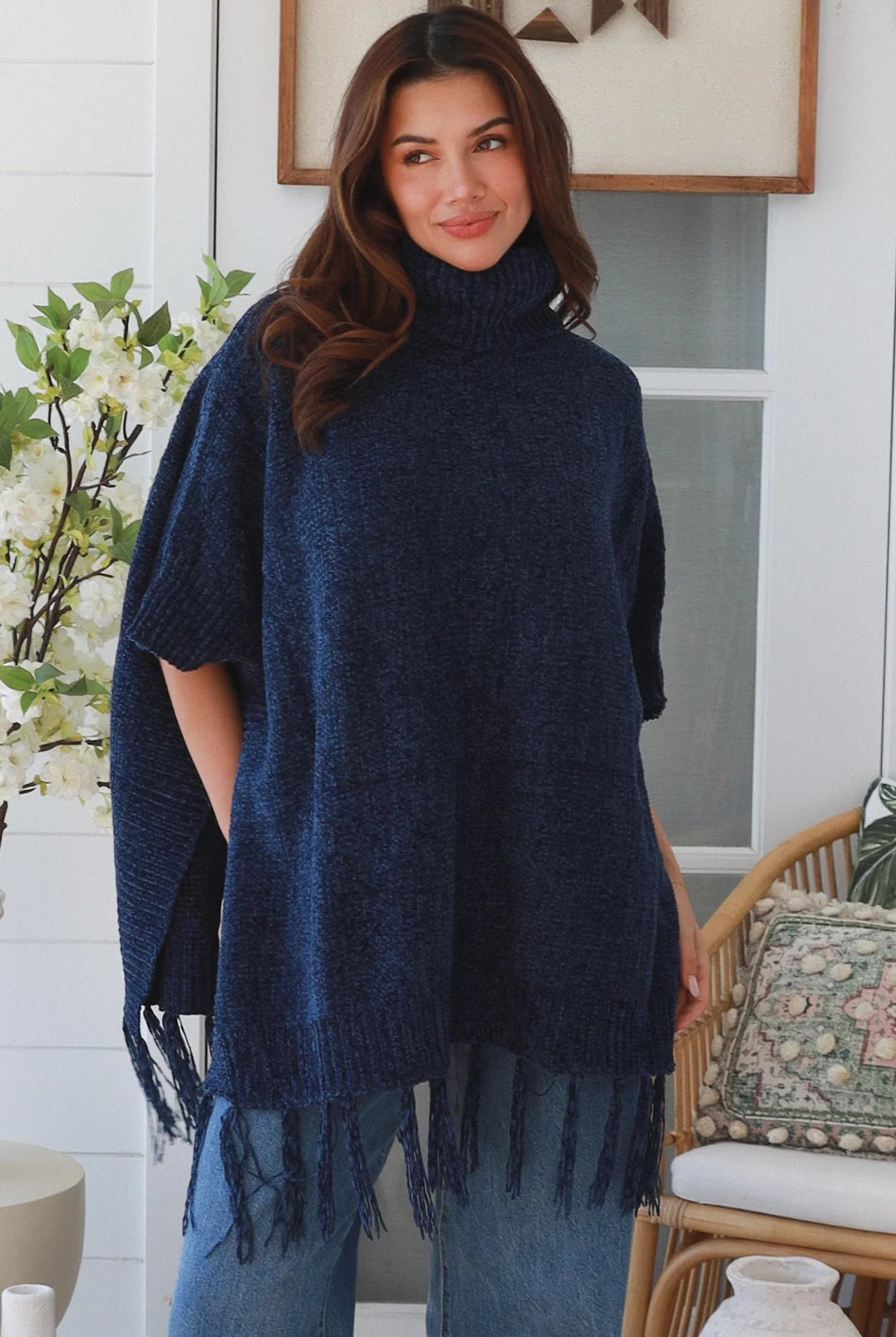 Woman wearing navy roll neck knit poncho with fringe hem and relaxed winter boho styling