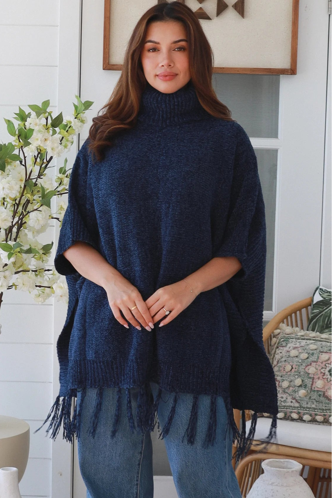 Woman wearing navy roll neck knit poncho with fringe hem and relaxed winter boho styling