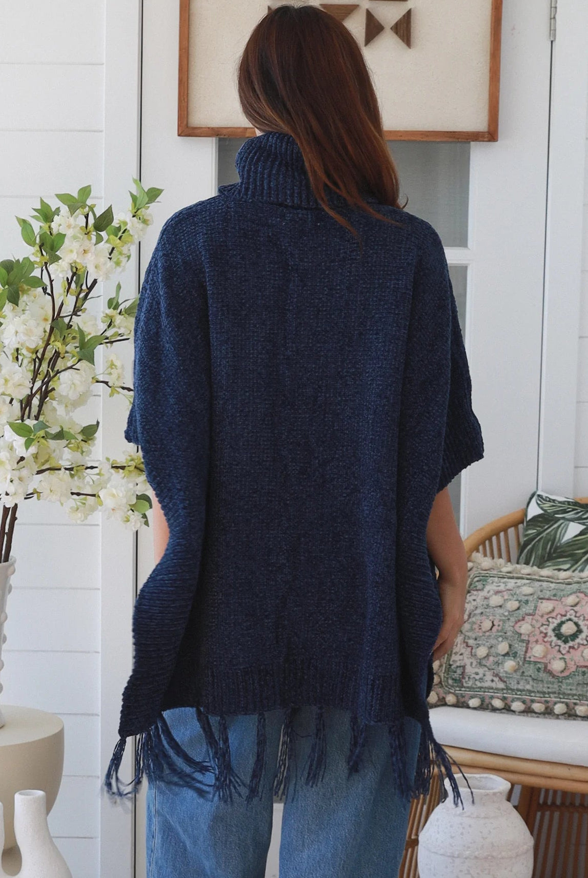 Woman wearing navy roll neck knit poncho with fringe hem and relaxed winter boho styling