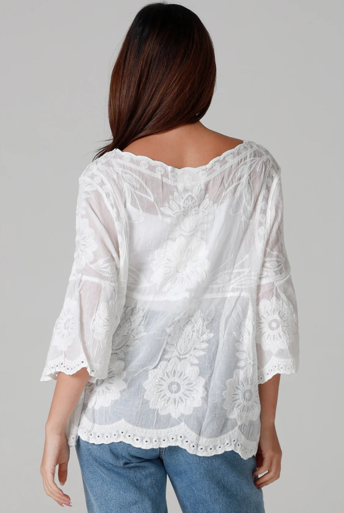 Woman wearing a white cotton embroidered boho blouse with scalloped neckline and flared sleeves styled with denim jeans - Fleur Belle Blouse Australia.