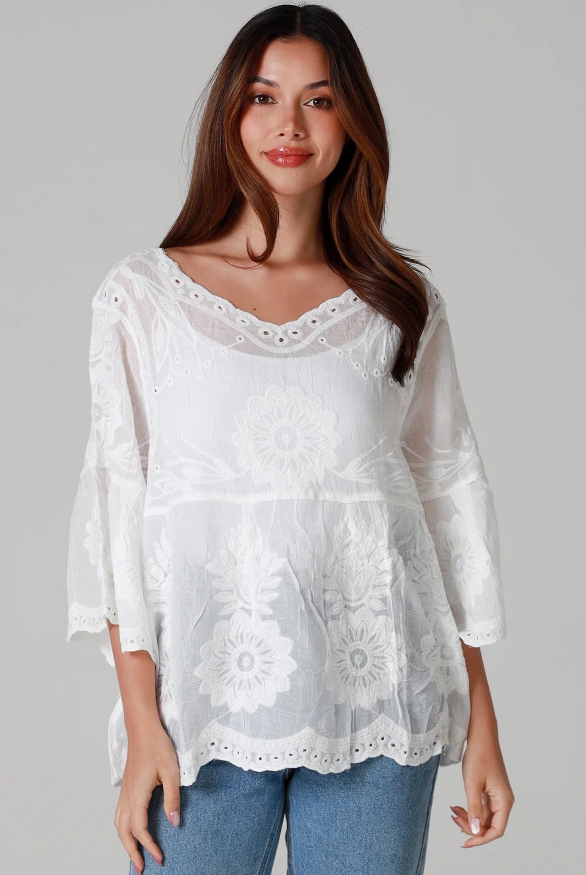 Woman wearing a white cotton embroidered boho blouse with scalloped neckline and flared sleeves styled with denim jeans - Fleur Belle Blouse Australia.