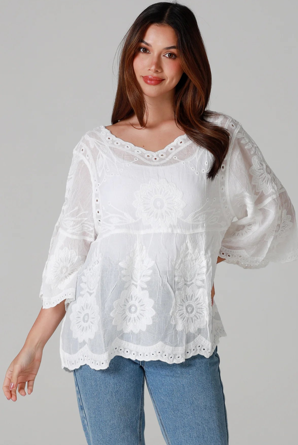 Woman wearing a white cotton embroidered boho blouse with scalloped neckline and flared sleeves styled with denim jeans - Fleur Belle Blouse Australia.