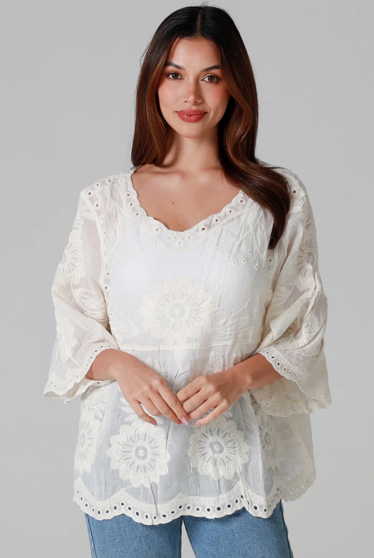 Woman wearing a cream embroidered cotton blouse with flared sleeves and scalloped neckline styled with jeans - Fleur Belle Blouse Australia.
