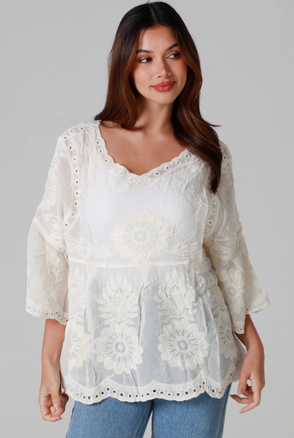 Woman wearing a cream embroidered cotton blouse with flared sleeves and scalloped neckline styled with jeans - Fleur Belle Blouse Australia.
