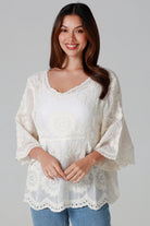 Woman wearing a cream embroidered cotton blouse with flared sleeves and scalloped neckline styled with jeans - Fleur Belle Blouse Australia.