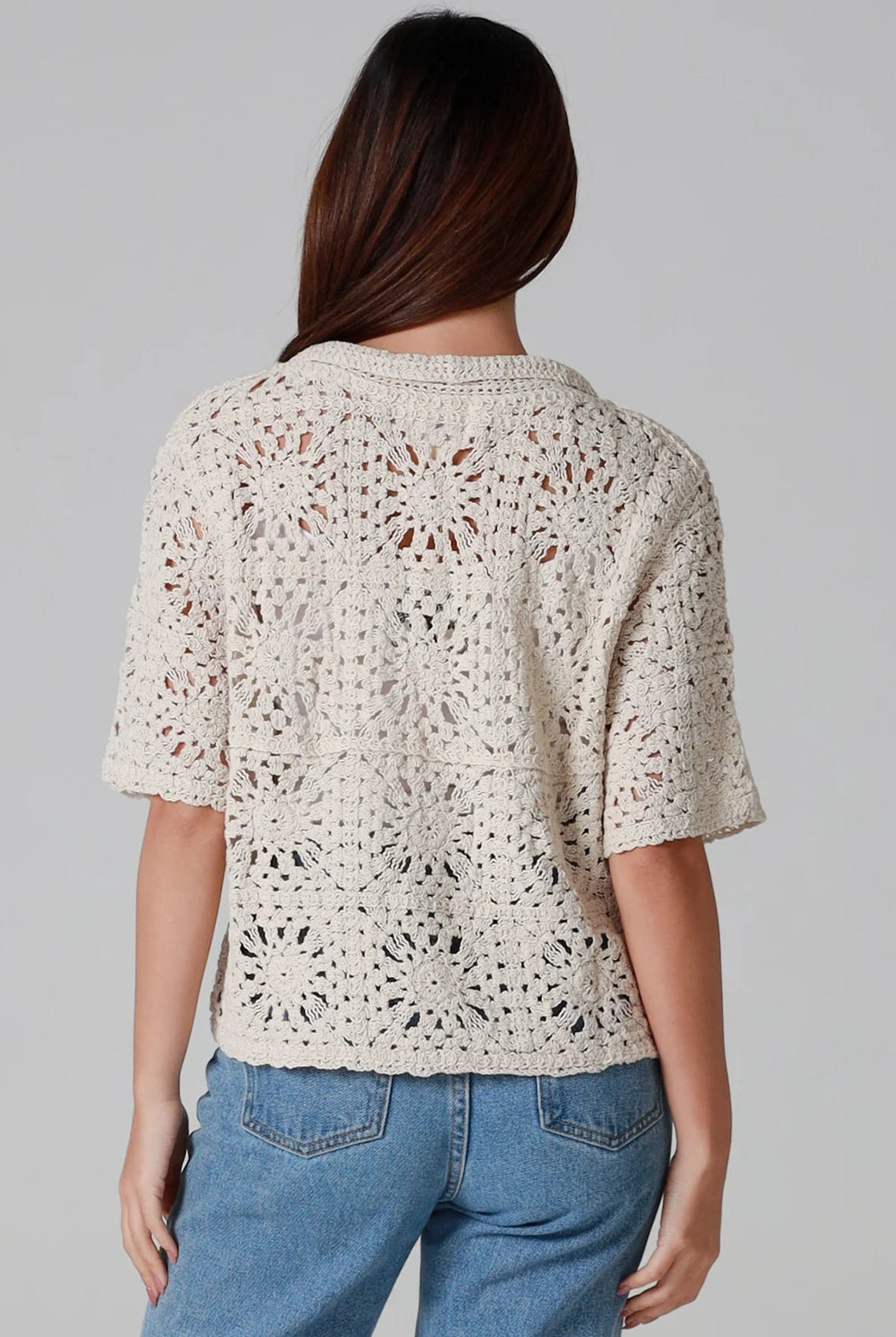 Woman wearing a beige short-sleeve crochet blouse with scalloped collar and buttons, styled open over jeans - boho cardigan top Australia.