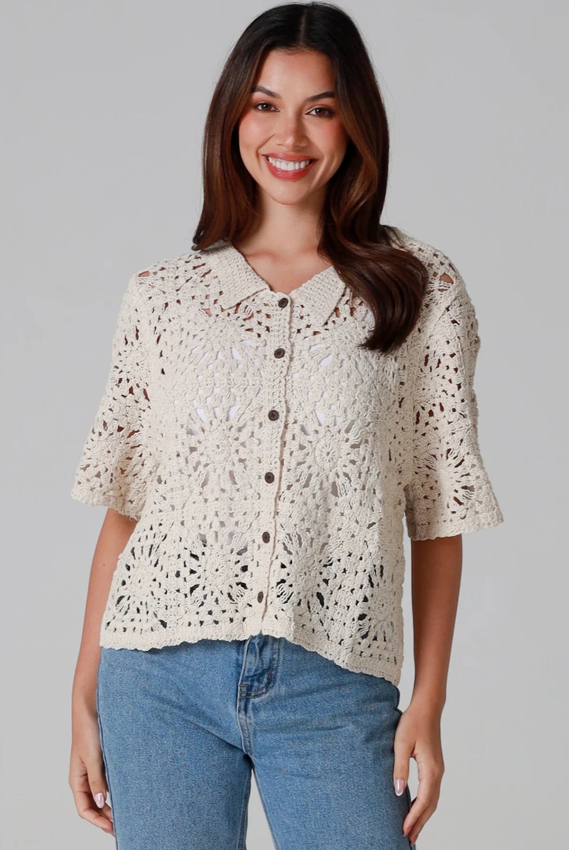 Woman wearing a beige short-sleeve crochet blouse with scalloped collar and buttons, styled open over jeans - boho cardigan top Australia.