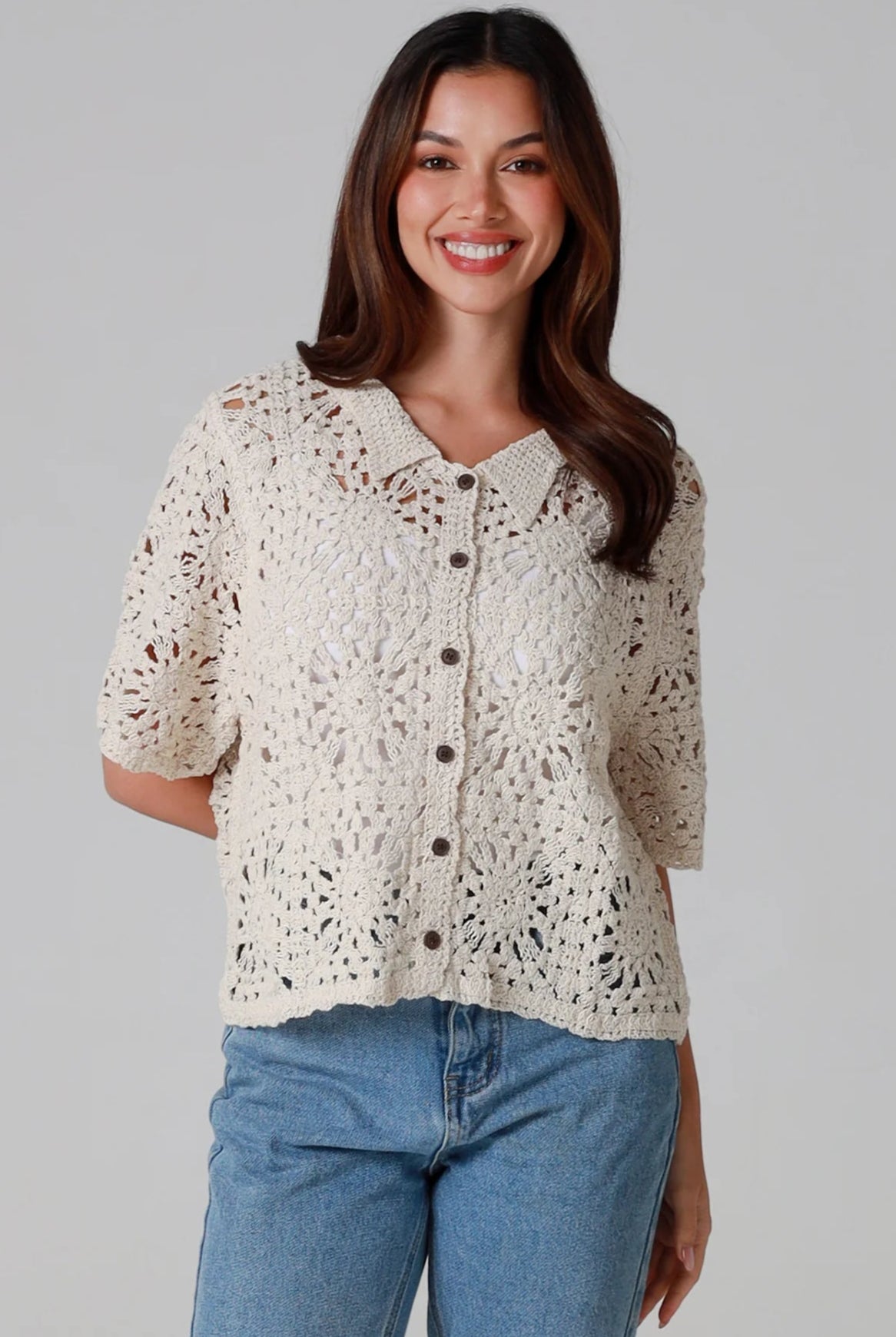 Woman wearing a beige short-sleeve crochet blouse with scalloped collar and buttons, styled open over jeans - boho cardigan top Australia.