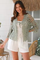 Woman wearing a sage green crochet cotton cardigan with floral and diamond pattern and scalloped sleeves - boho fashion Australia