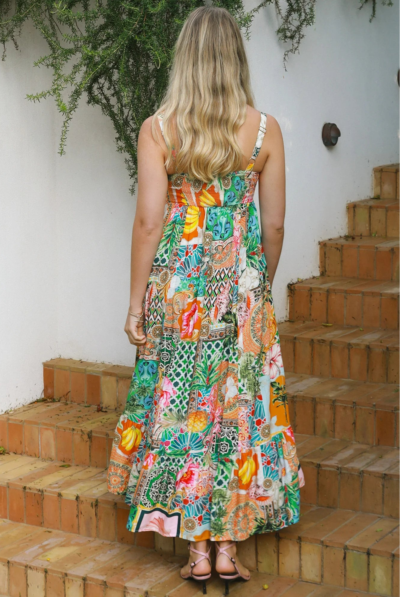 Woman in colourful ankle-sweeping island-print boho maxi dress with frill hemline and adjustable straps in bright summer.