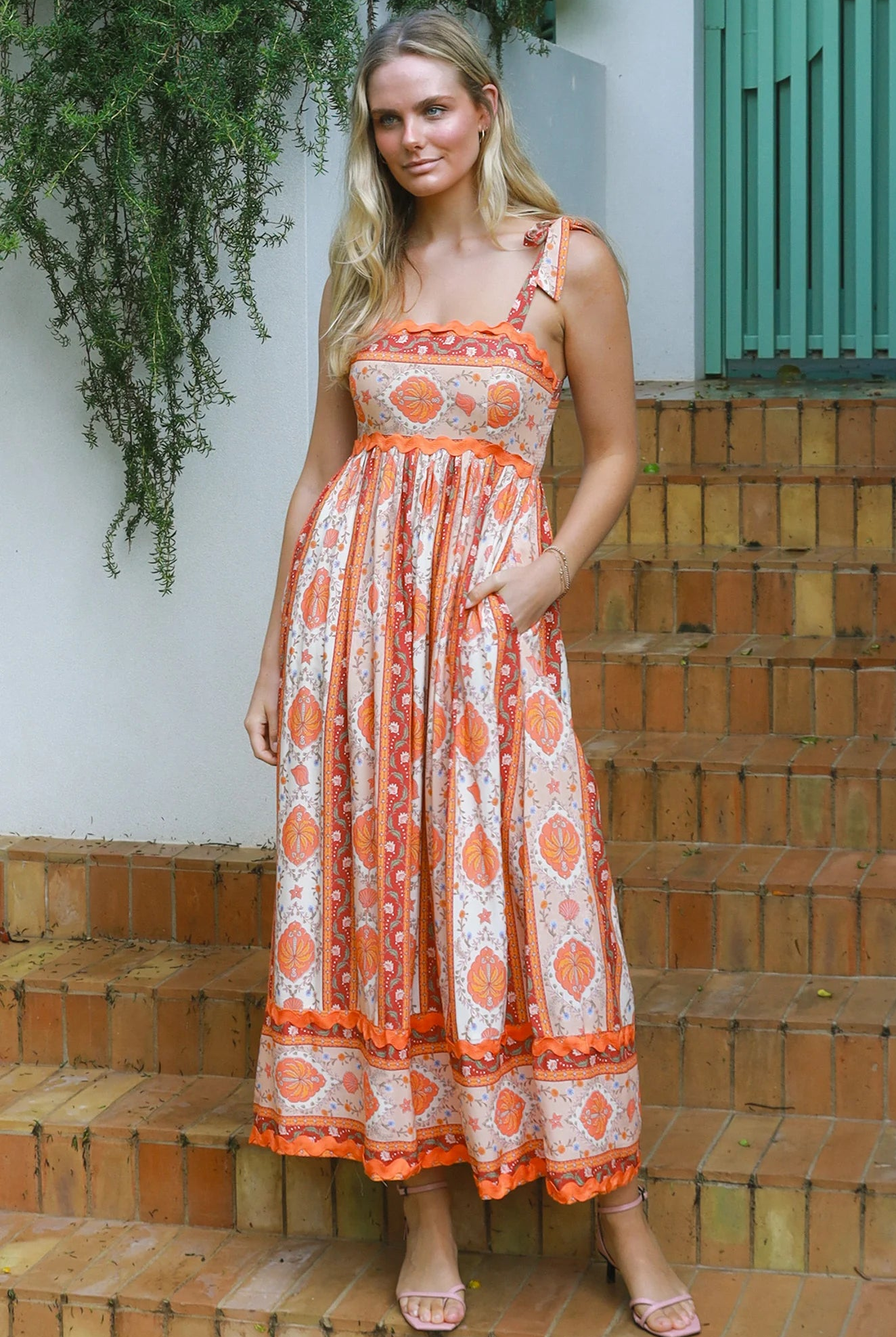 Woman wearing a sunset-coloured ankle-length maxi dress with shoulder ties and zigzag trim – Sundown Spice Maxi Dress.