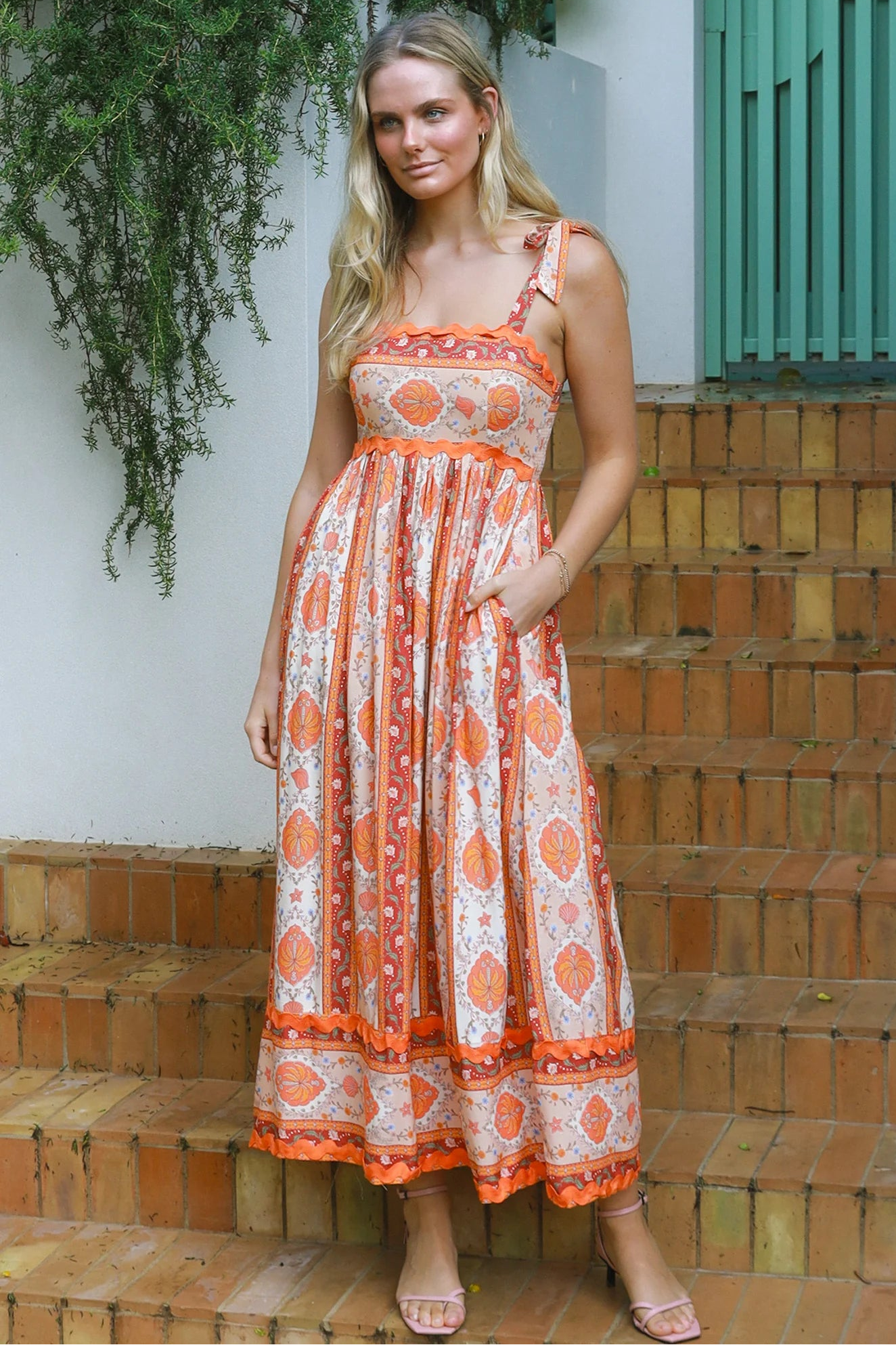 Woman wearing a sunset-coloured ankle-length maxi dress with shoulder ties and zigzag trim – Sundown Spice Maxi Dress.