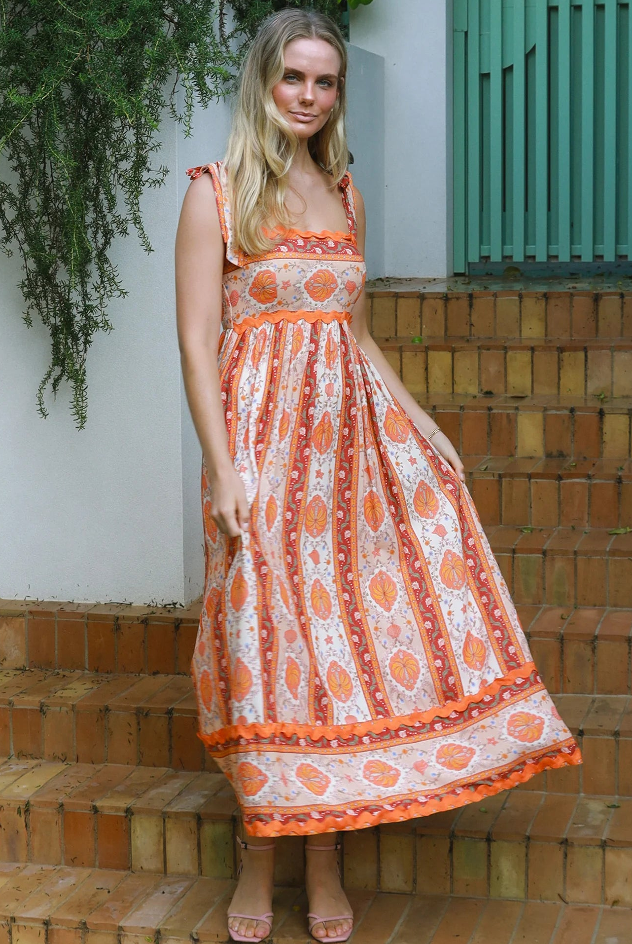 Woman wearing a sunset-coloured ankle-length maxi dress with shoulder ties and zigzag trim – Sundown Spice Maxi Dress.