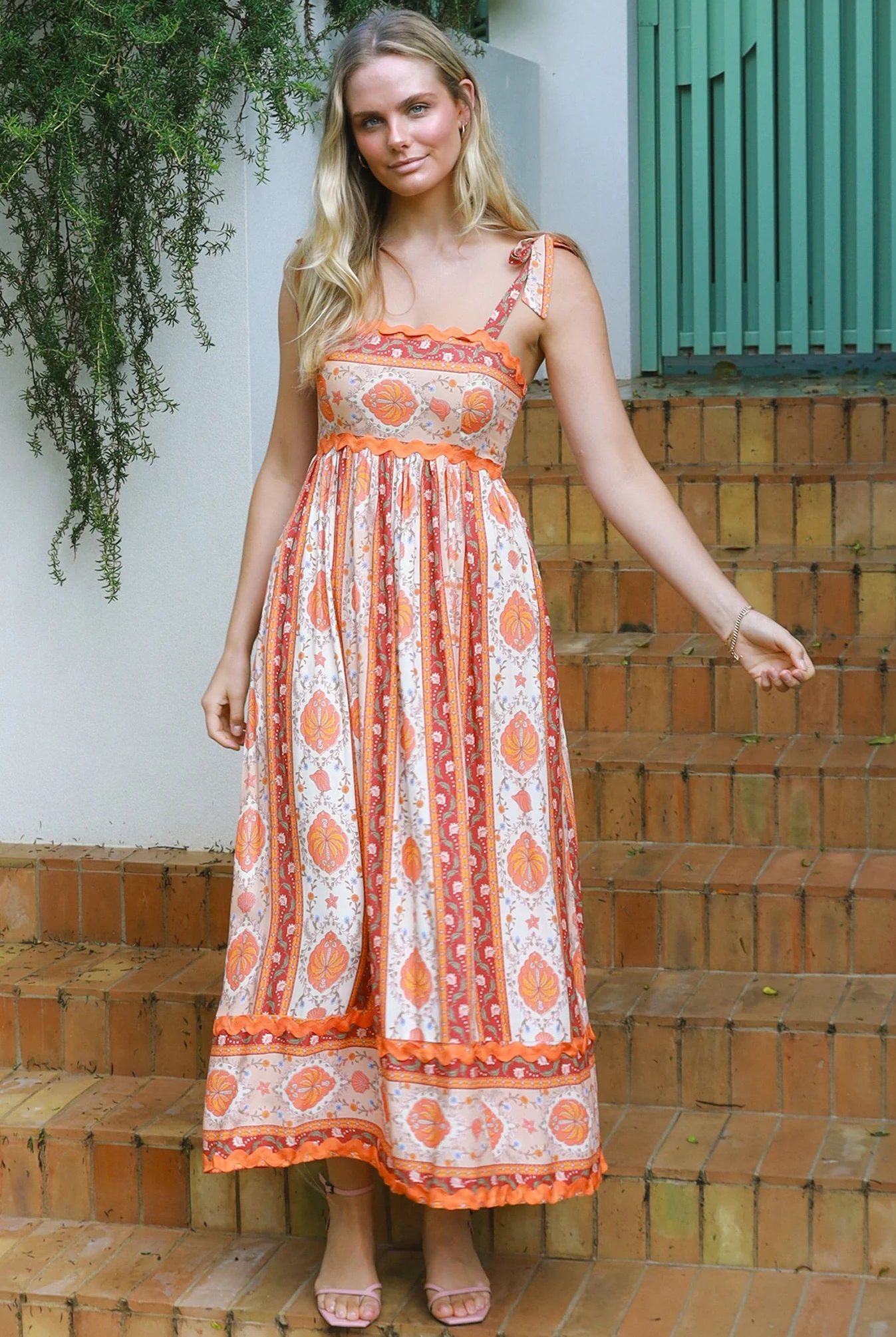 Woman wearing a sunset-coloured ankle-length maxi dress with shoulder ties and zigzag trim – Sundown Spice Maxi Dress.