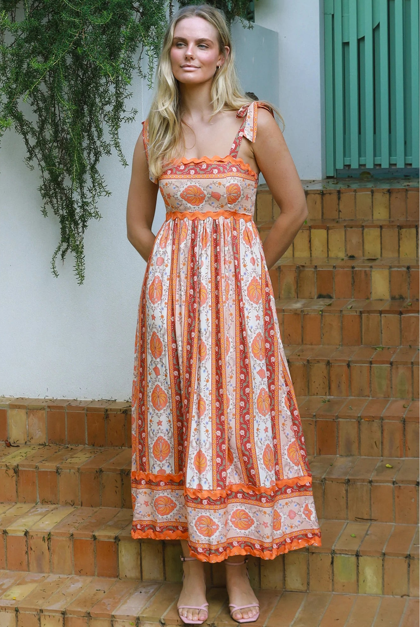 Woman wearing a sunset-coloured ankle-length maxi dress with shoulder ties and zigzag trim – Sundown Spice Maxi Dress.