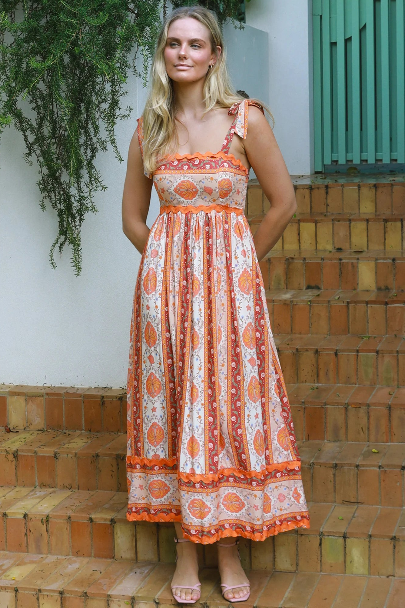 Woman wearing a sunset-coloured ankle-length maxi dress with shoulder ties and zigzag trim – Sundown Spice Maxi Dress.