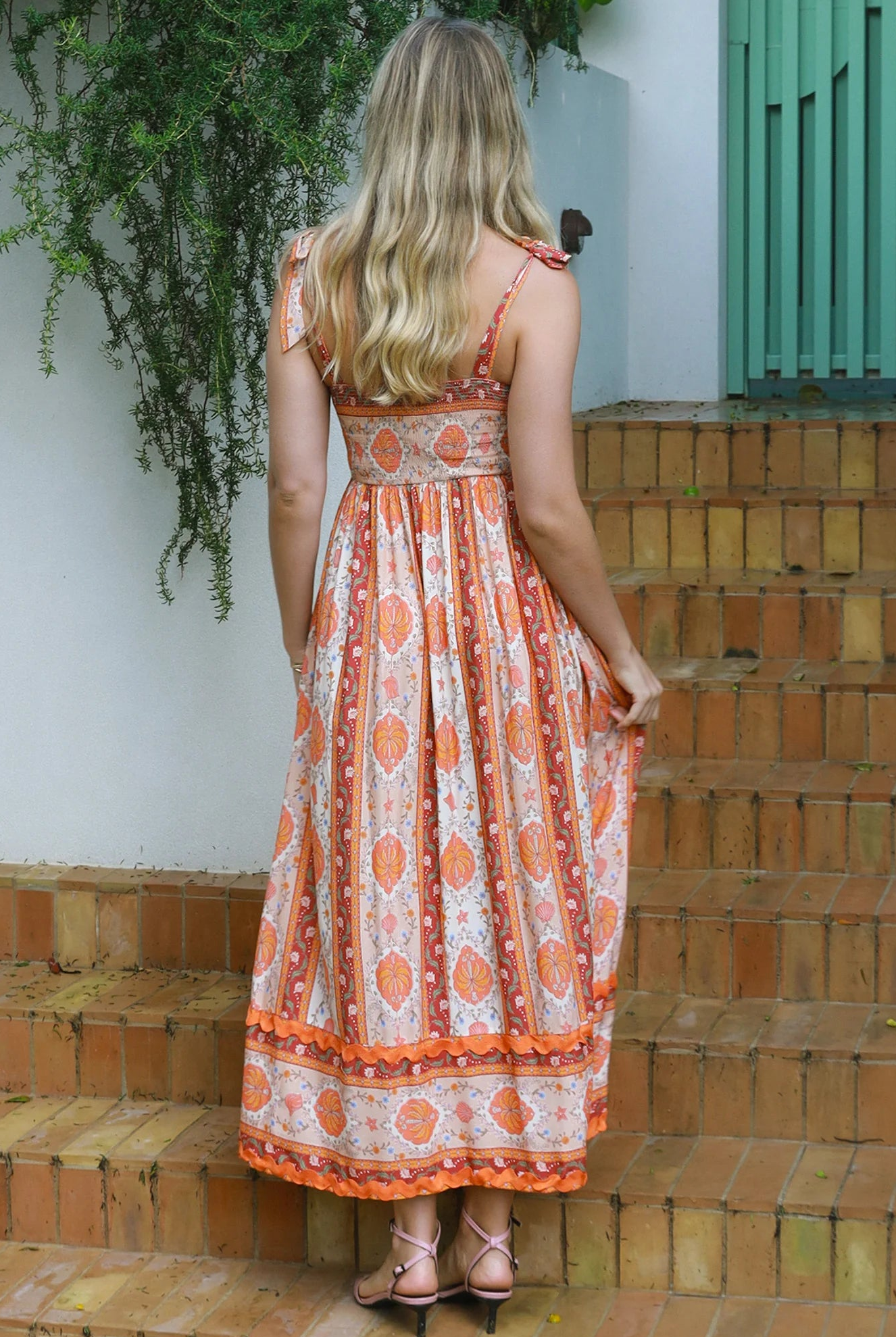 Woman wearing a sunset-coloured ankle-length maxi dress with shoulder ties and zigzag trim – Sundown Spice Maxi Dress.