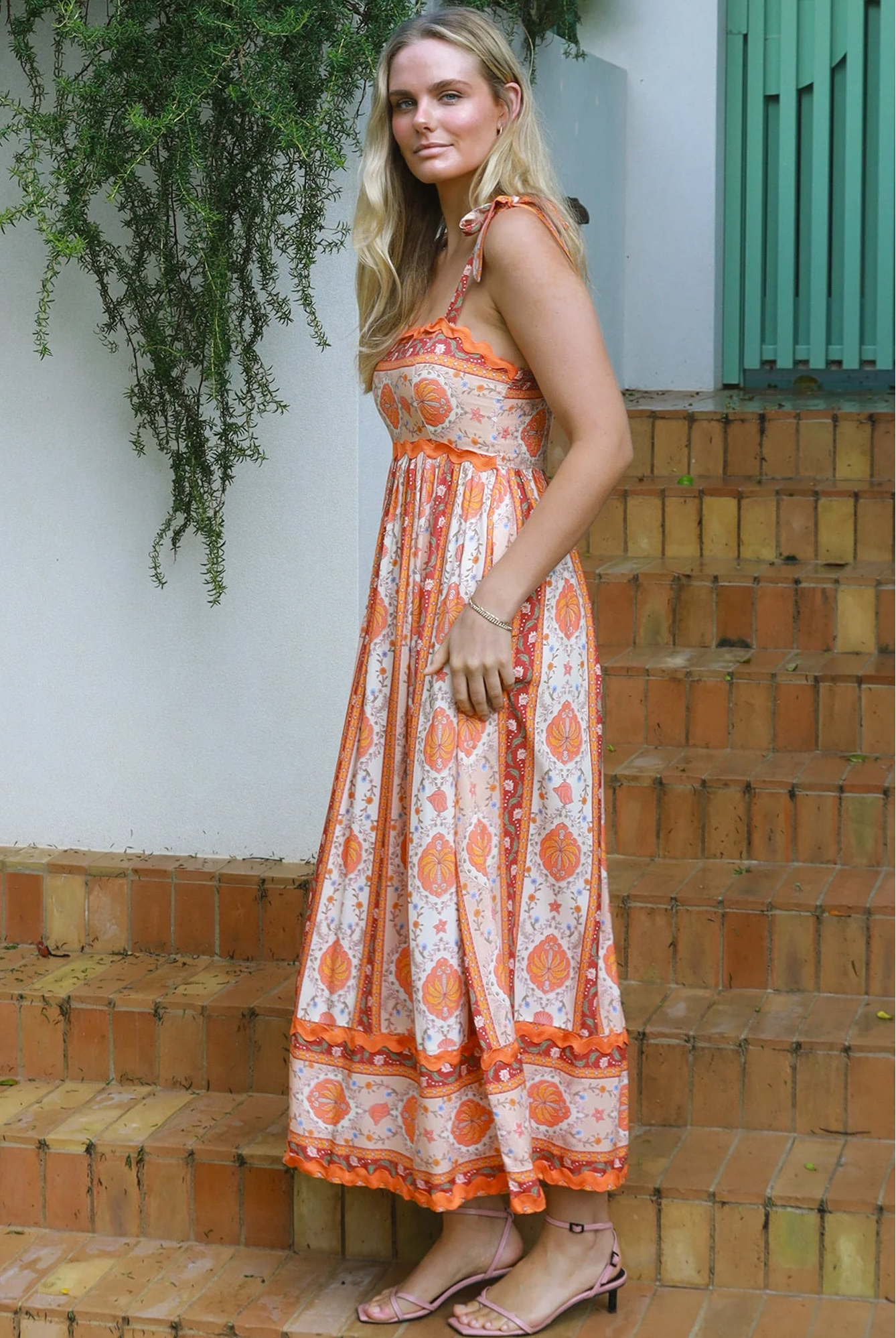 Woman wearing a sunset-coloured ankle-length maxi dress with shoulder ties and zigzag trim – Sundown Spice Maxi Dress.