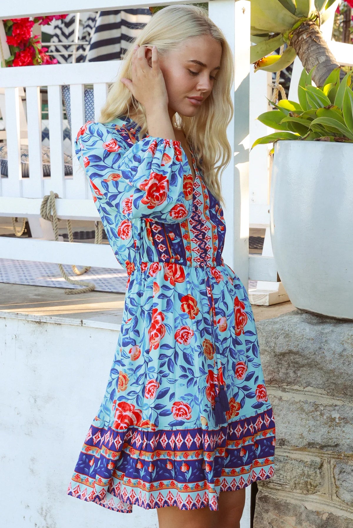 Blonde woman in blue floral boho mini dress with red roses and border print details - Clarice Rose Mini Dress Bohemian Love Runway.