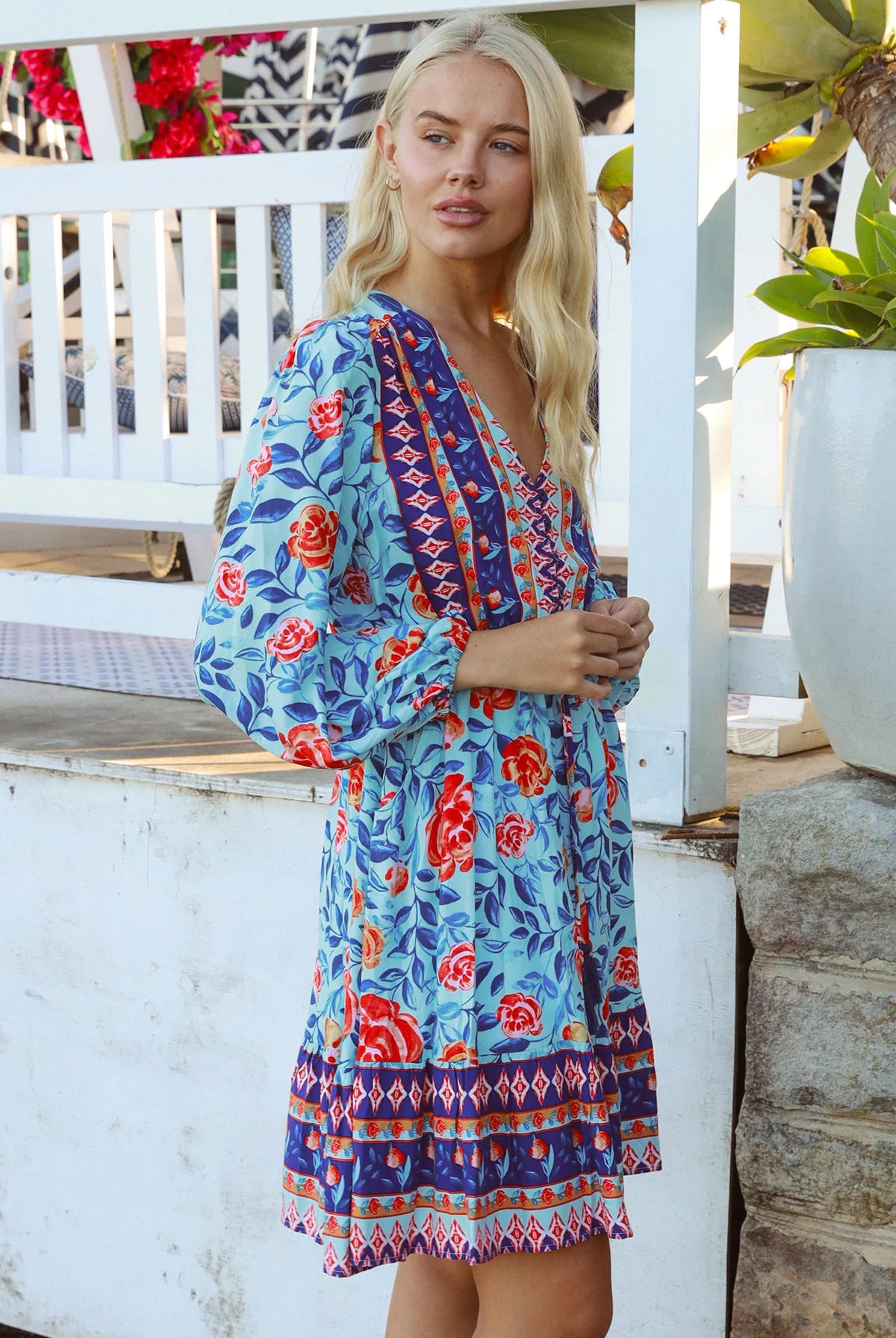Blonde woman in blue floral boho mini dress with red roses and border print details - Clarice Rose Mini Dress Bohemian Love Runway.