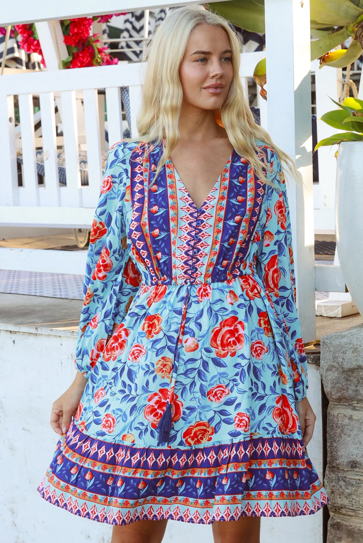 Blonde woman in blue floral boho mini dress with red roses and border print details - Clarice Rose Mini Dress Bohemian Love Runway.